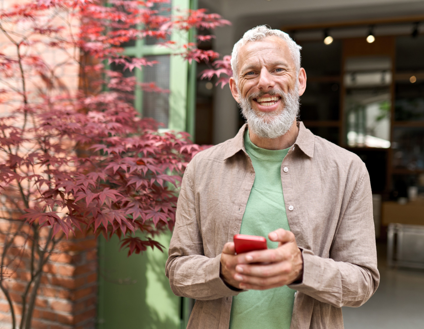 A greying happy man is checking his phone, while looking to the camera