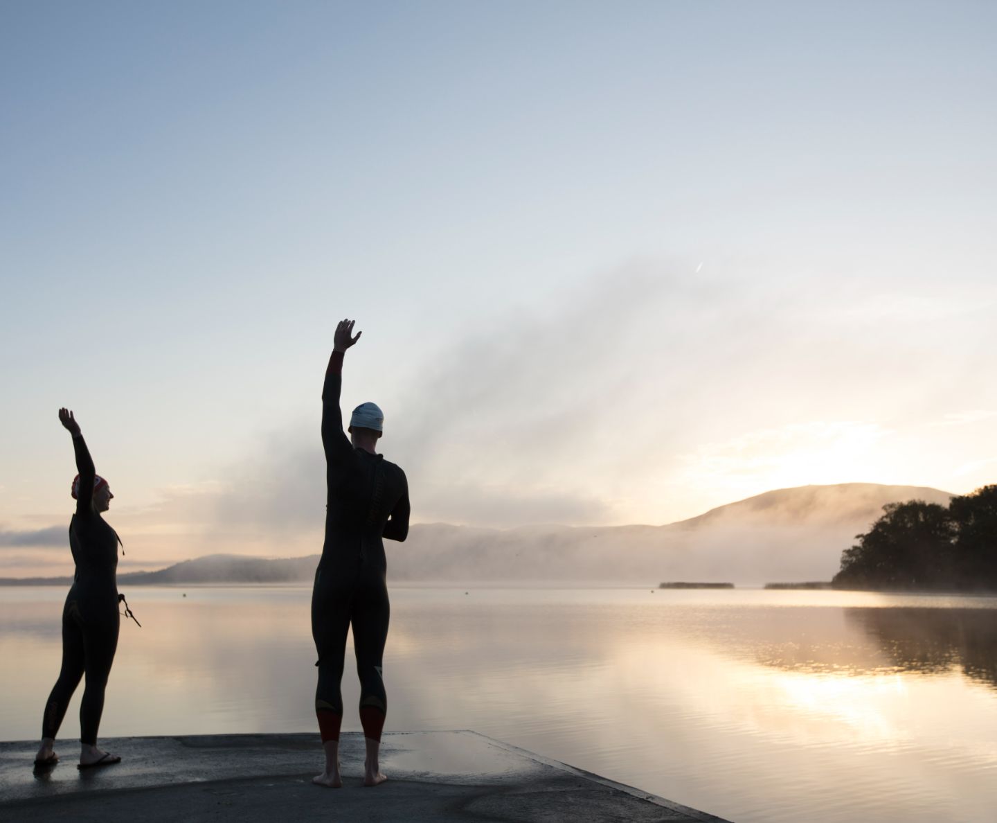Two swimmers stretching as the sun rises over the lake