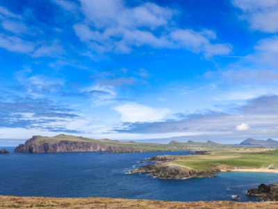 A scenic view of Dingle Bay with blue water, green land, and distant hills under a bright sky.