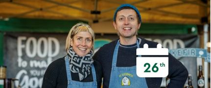 Two people in front of stalls with a calendar that reads 26