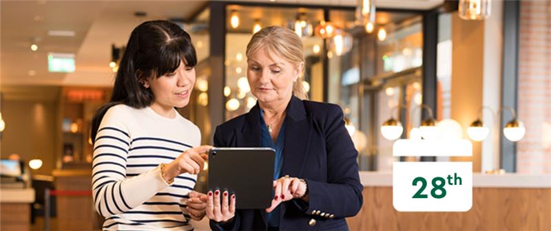 Two women looking at a tablet and a calendar that reads 28th