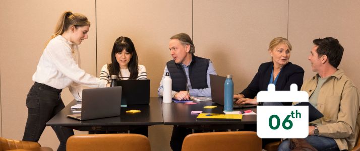 Team of colleagues sitting at a desk, calendar icon reads 6th